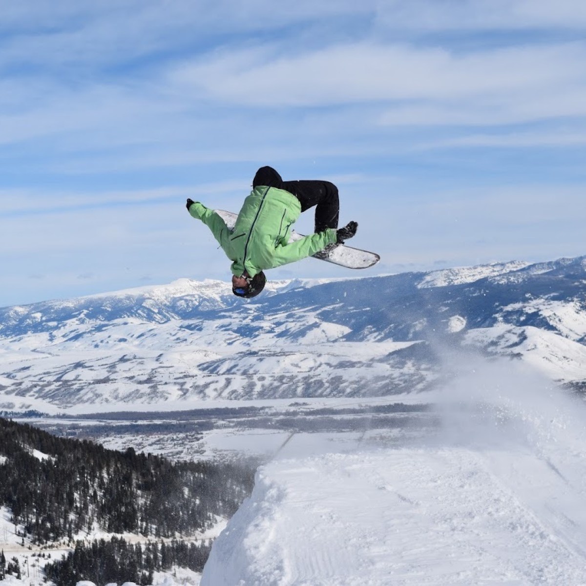 a man flying through the air while riding a snowboard down a snowy hill