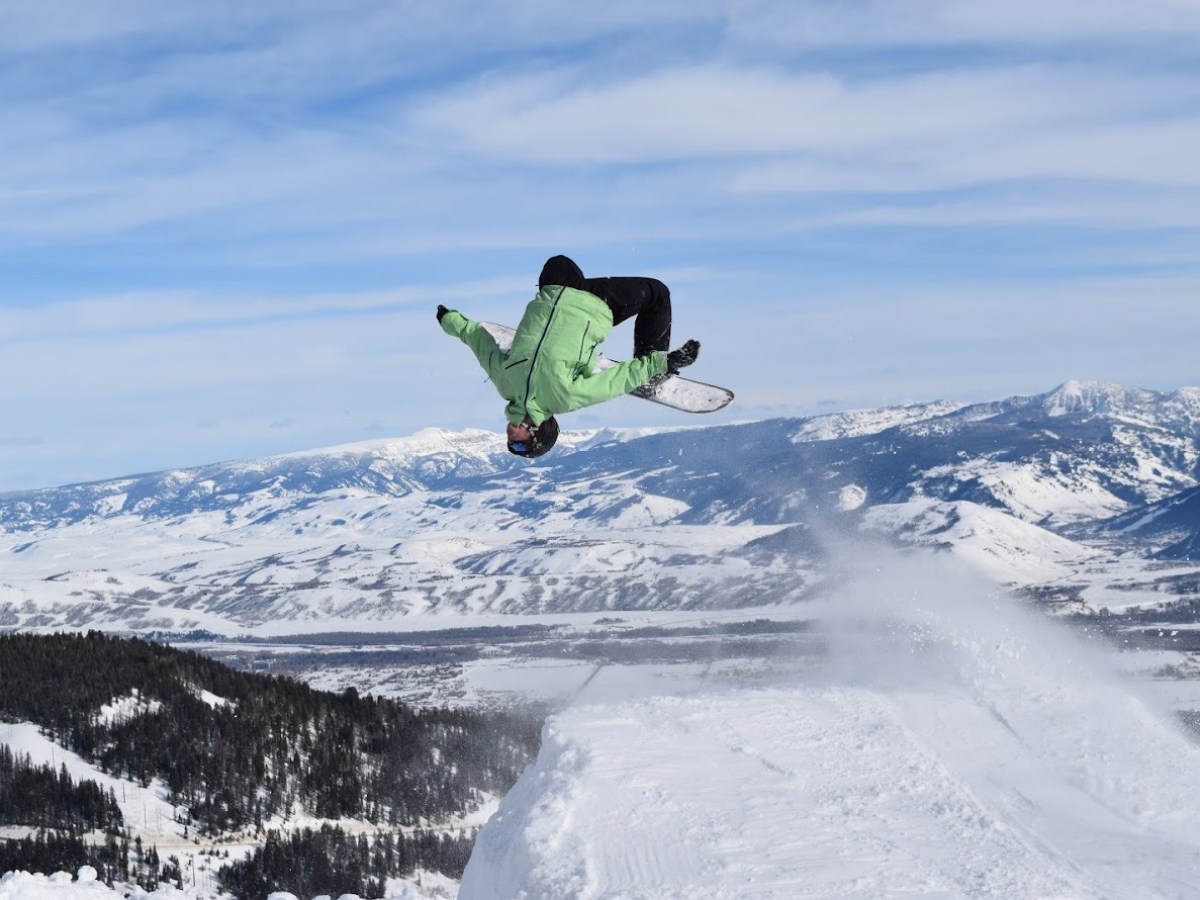 a man flying through the air while riding a snowboard down a snowy hill