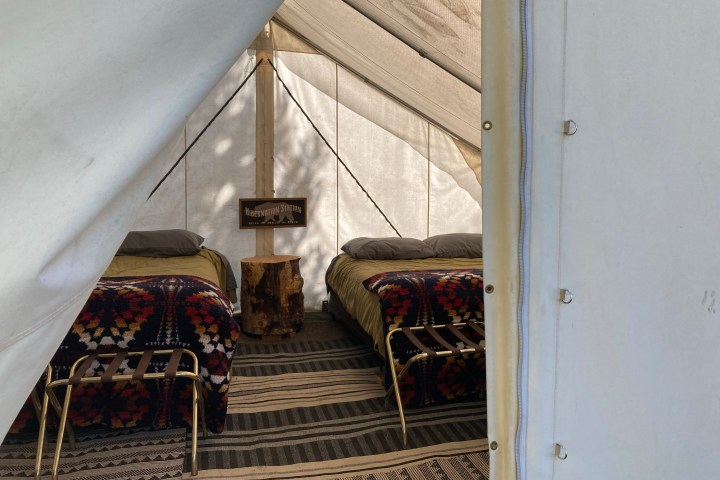 Inside view of a tent with two beds, patterned blankets, and a central wooden stump table.