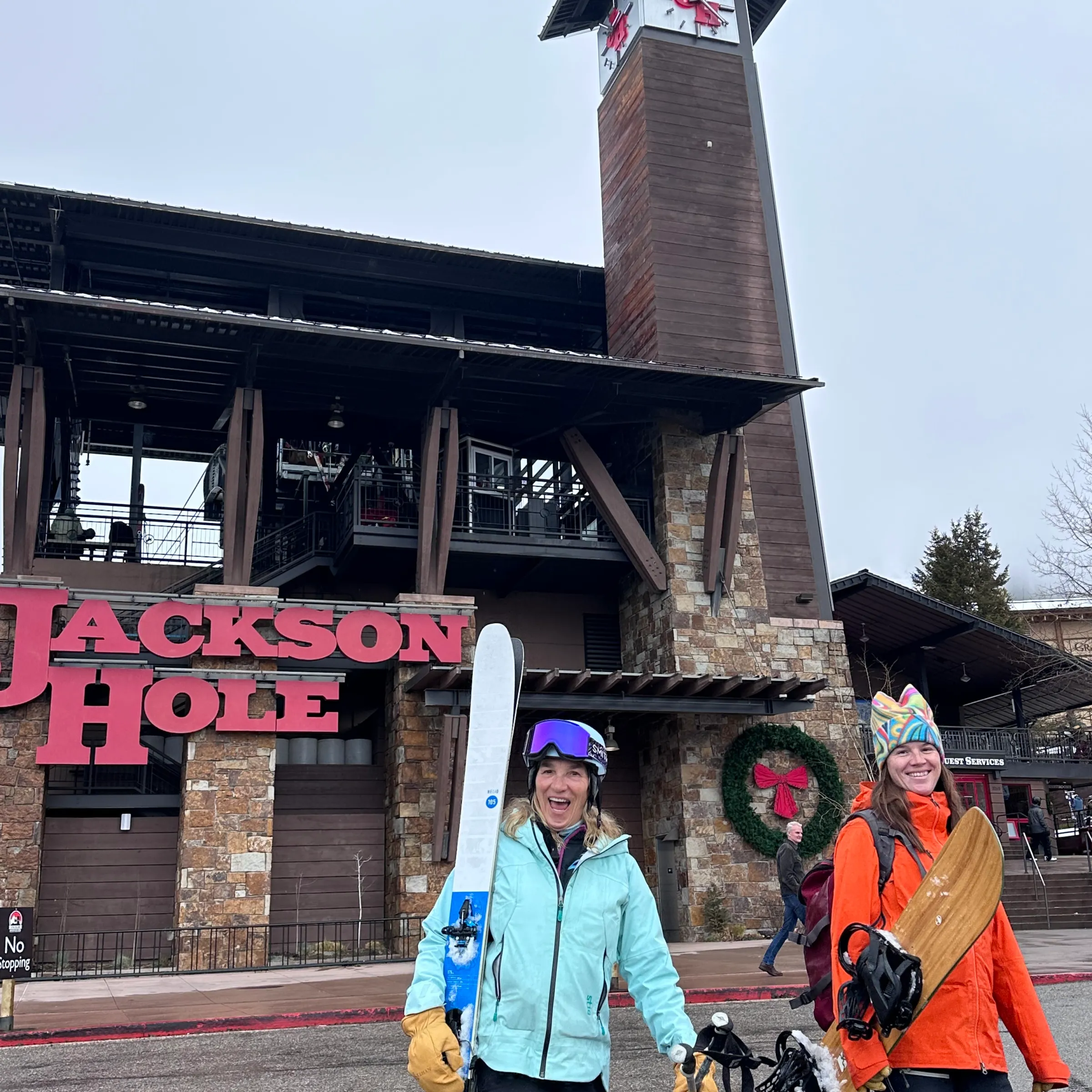 Two people with ski gear outside Jackson Hole building on a cloudy day.