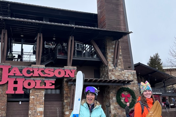Two people with ski gear outside Jackson Hole building on a cloudy day.